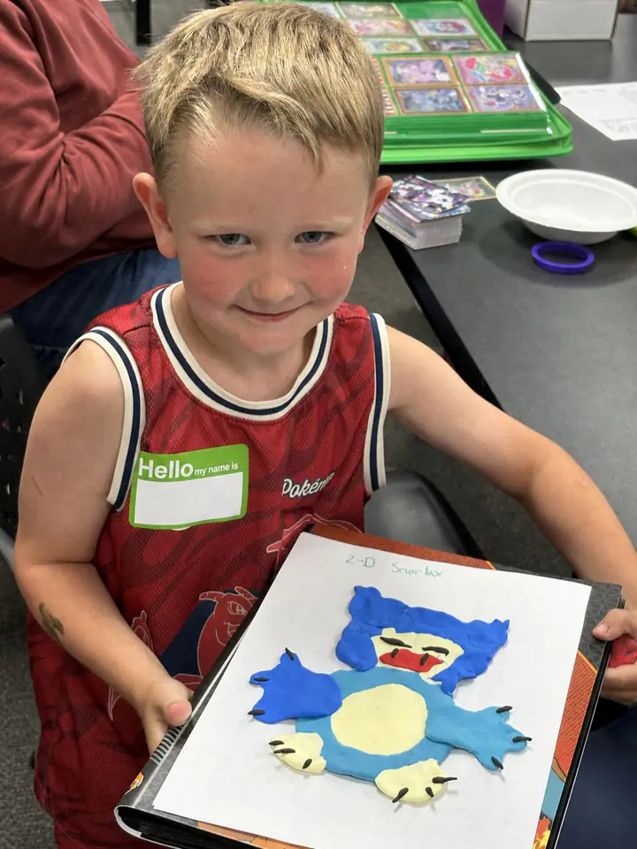 A child holds up a handmade Pokémon craft during Grandma Jane's Kids Club at Izzi's Gym